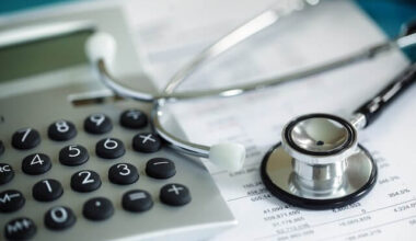 Calculator and stethoscope on top of a spreadsheet depicting health insurance premiums/costs