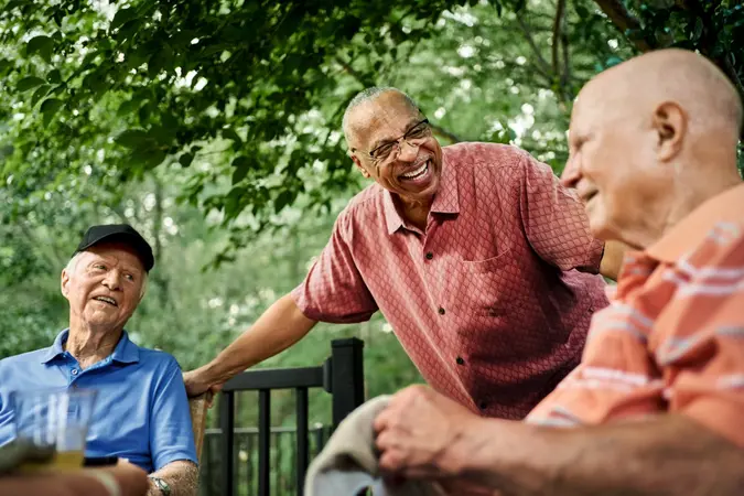 Group of happy senior male residents gathered around a table in the backyard of a retirement home, engaging in conversation and enjoying the serene outdoor space.