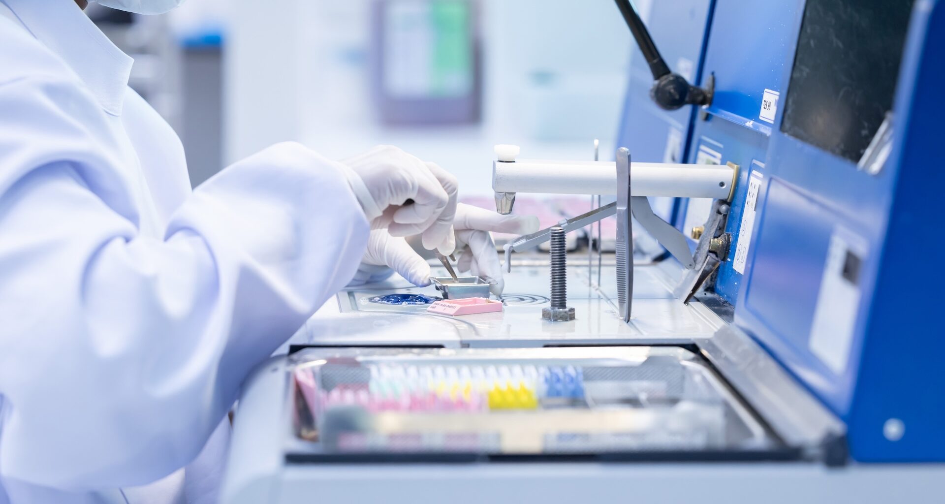 A lab technician in gloves uses tweezers to handle samples on a clean workstation.