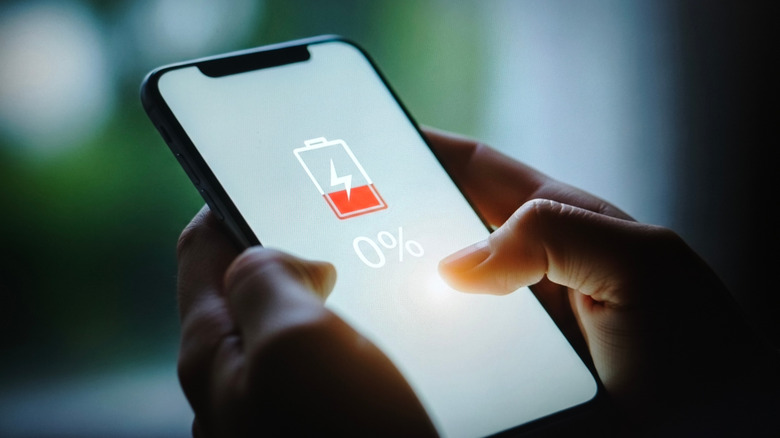 a person holding a smartphone showing the 0% battery symbol on it
