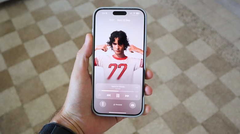 A hand holding the iPhone 16 Pro Max with Apple Music's animated cover for the Lock Screen