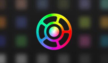 A circular logo with a black center and radiating segments, outlined in a gradient of bright rainbow colors, set against a blurred dark background featuring faint colored squares.