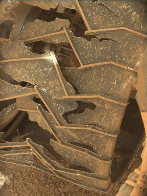 Close-up of a cracked and damaged wheel with a zigzag tread pattern, covered in dust and dirt, likely from use in a rough, rocky terrain.