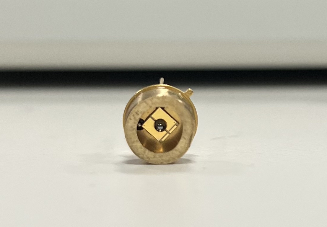 A close up of a circular brass-looking device with a square in the center of it and a light source in the center of that