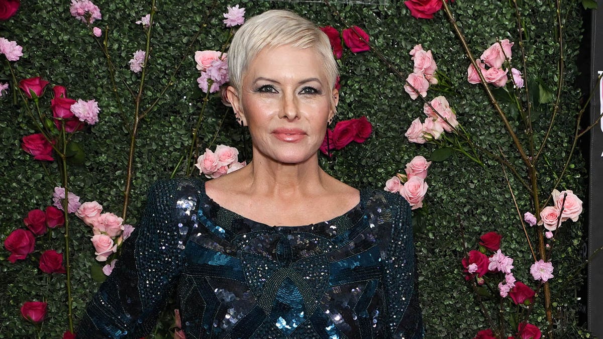Nicole Eggert is pictured posing in front of a hedge decorated with roses in April 2025.