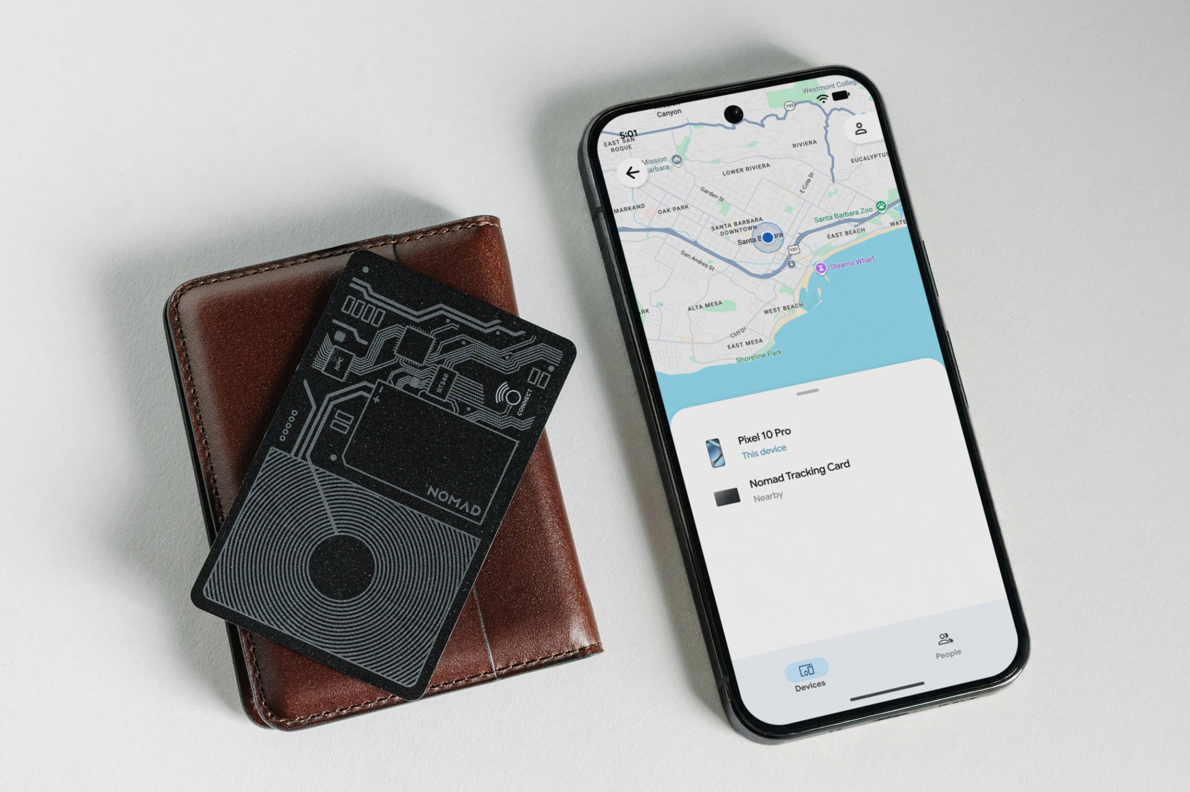 The Nomad Tracking Card Air sitting on a leather wallet next to an Android phone.