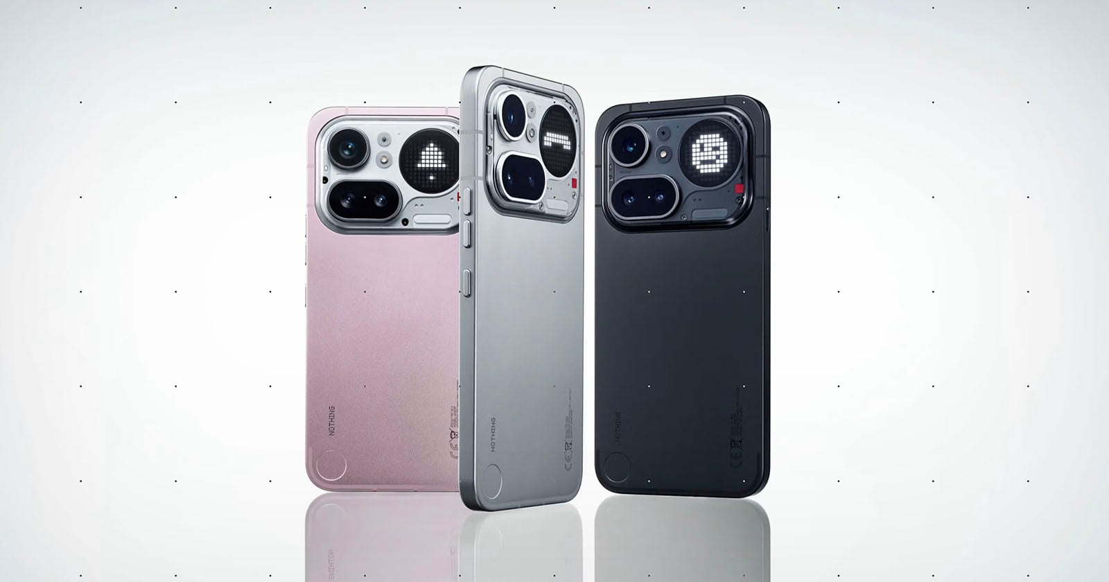 Three smartphones are standing upright side by side, displayed in pink, silver, and black colors. Each phone has a distinctive large camera module with multiple lenses and sensors on a minimalist back design.