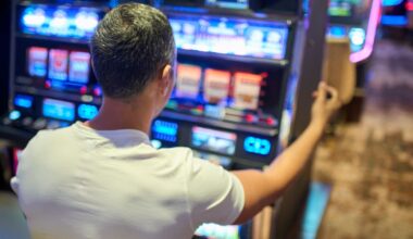 A view over the shoulder of a man wearing a white t-shirt with gray hair sitting at a slot machine
