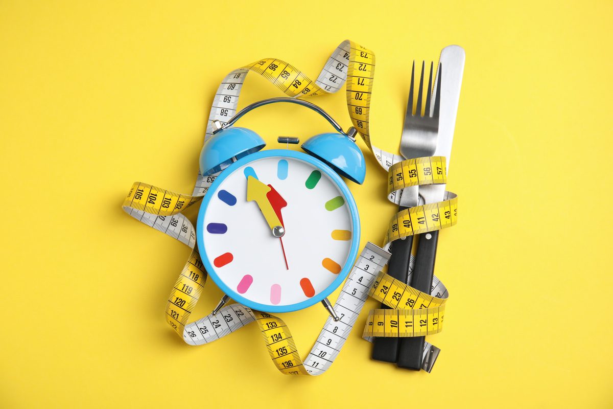 Alarm clock, measuring tape and cutlery on yellow background, flat lay