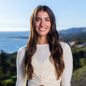 Woman smiles at camera with view of a bay behind her