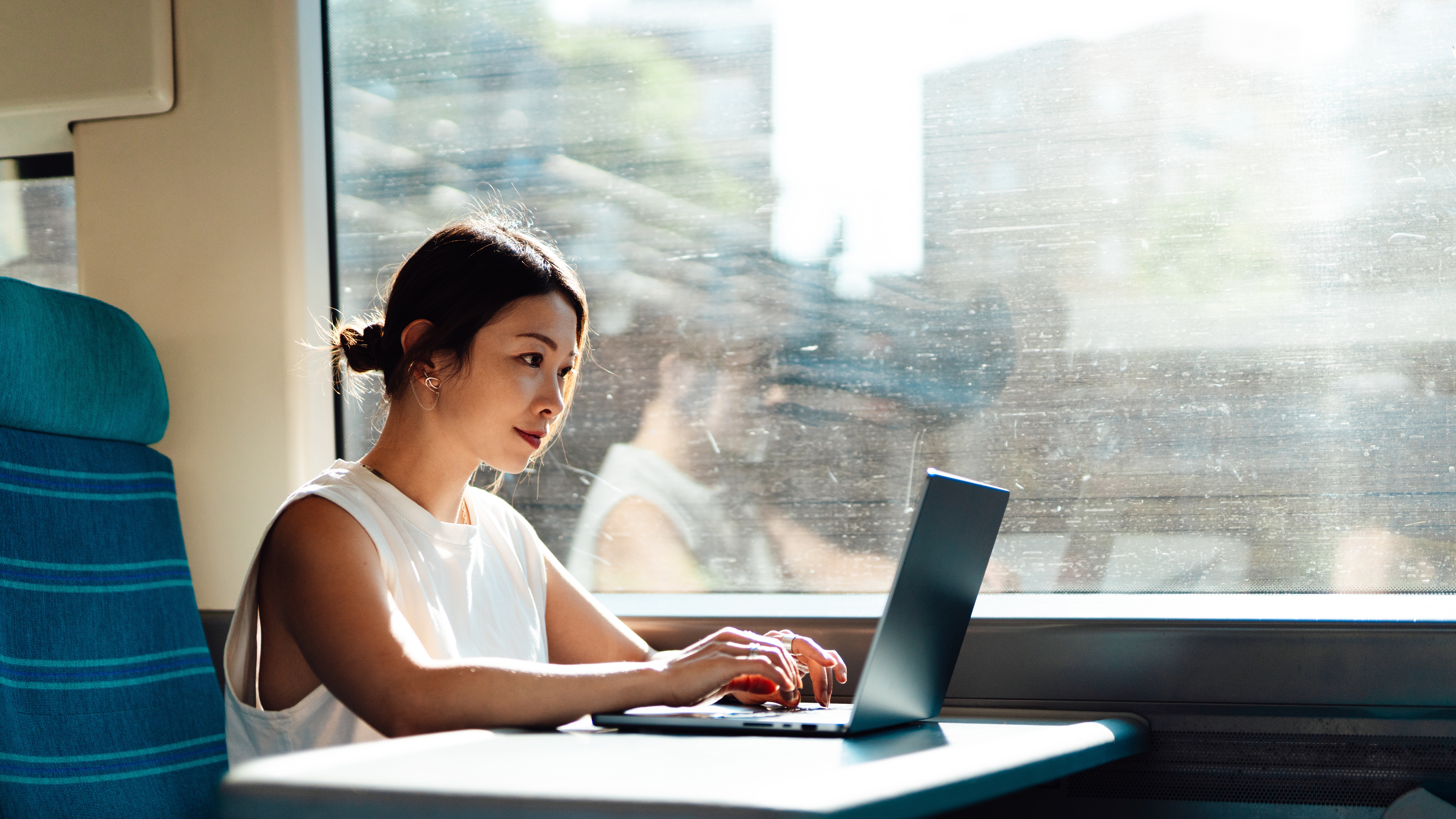 Young woman on a laptop on a train working, business and technology.