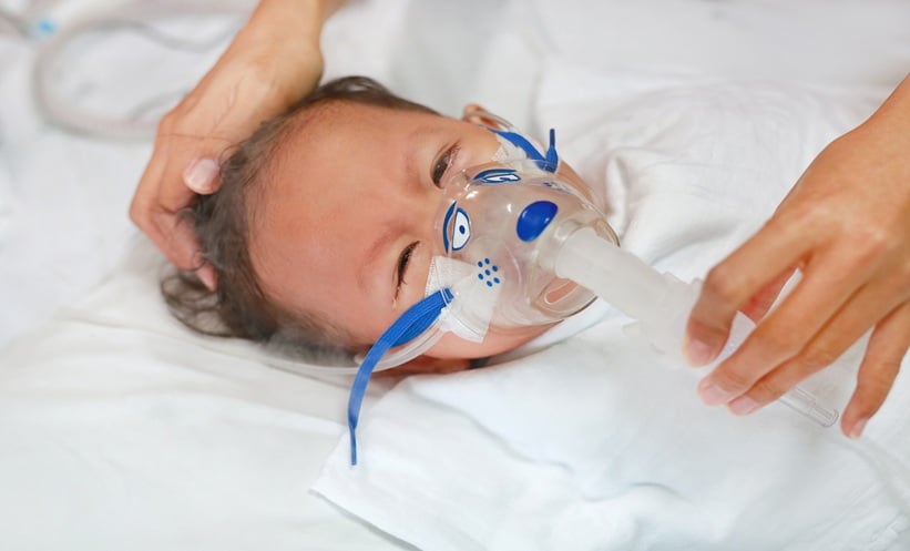 Sick baby boy on a hospital bed applying inhale medication to cure RSV.