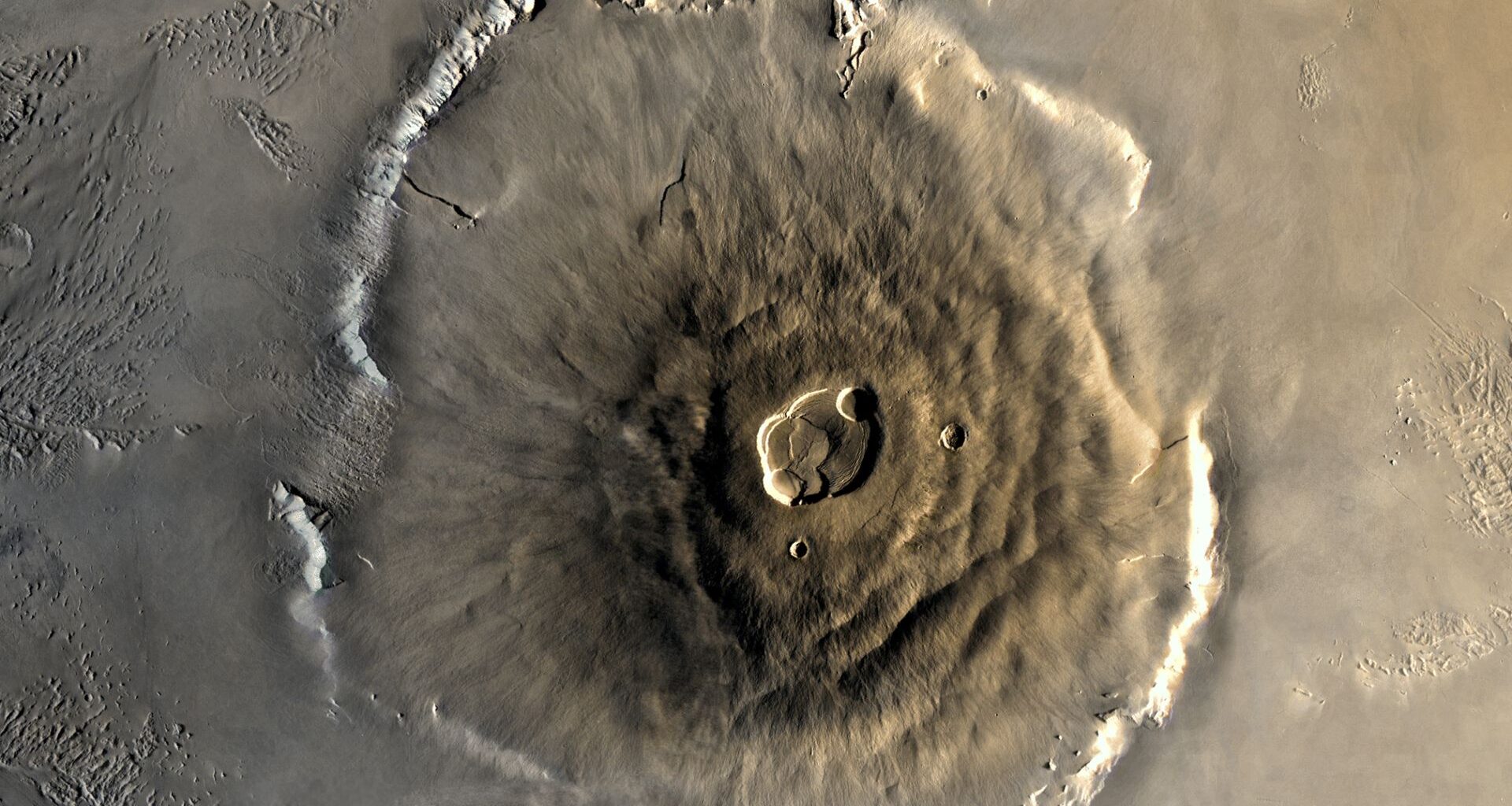 A close up of Olympus Mons on the surface of Mars, its structure a pile of brown lava in a large circular mount on the surface of the planet