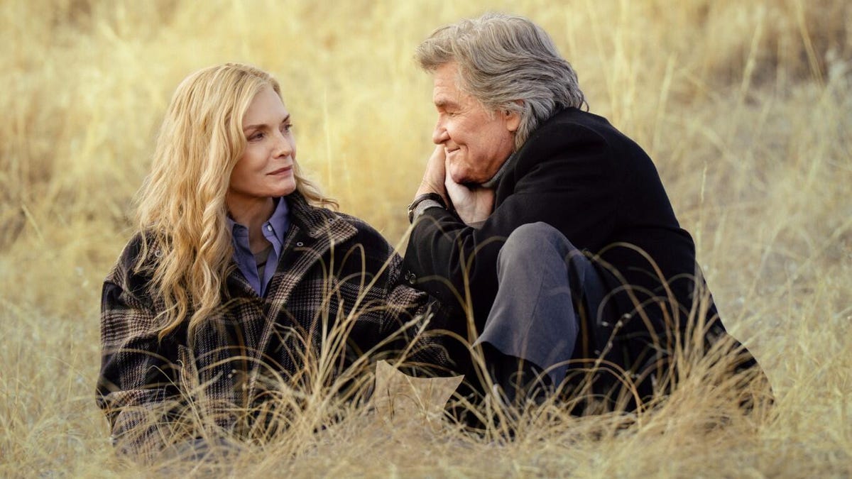 A production still from The Madison showing Michelle Pfeiffer and Kurt Russell sitting lovingly in a field.