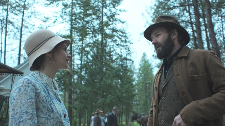 Felicity Jones's Gladys Olding Grainier talks to Joel Edgerton's Robert Grainier outside a church in a forest in Train Dreams