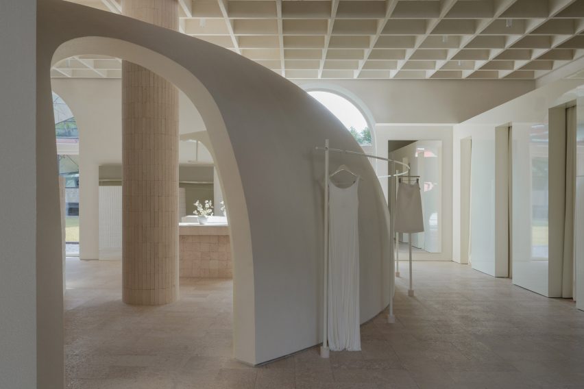 Image of a truncated domed partition wall with arched walkways connecting the main shop floor from a gloss-finished block of changing rooms at the far right of the image. A clothes rail with a hanging dress and skirt wraps around the dome's exterior.