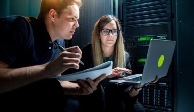 Two engineers, one writing in a notebook and the other using a laptop, are working in an AI data center.