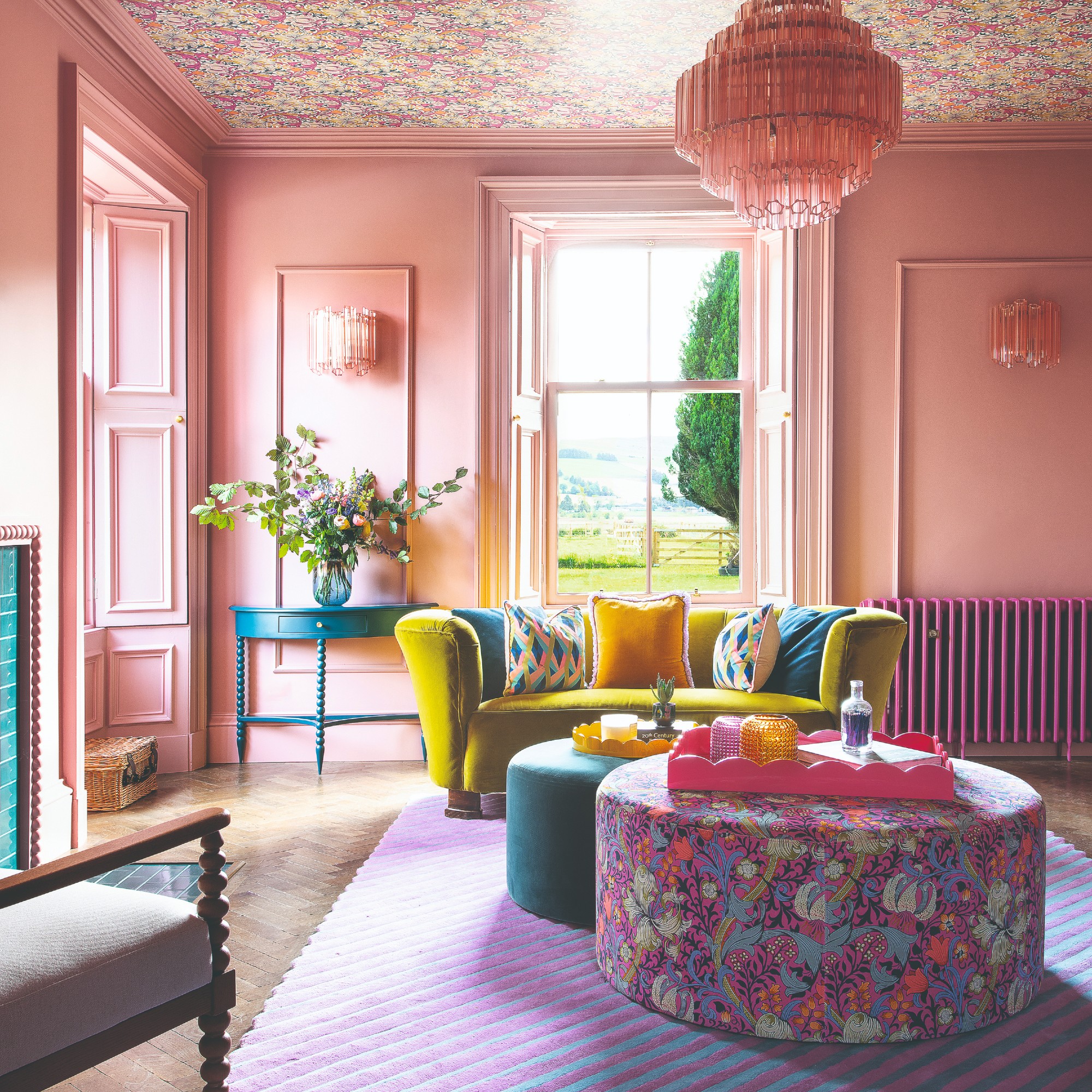 A living room with high ceilings painted pink and and the ceiling covered in a floral wallpaper