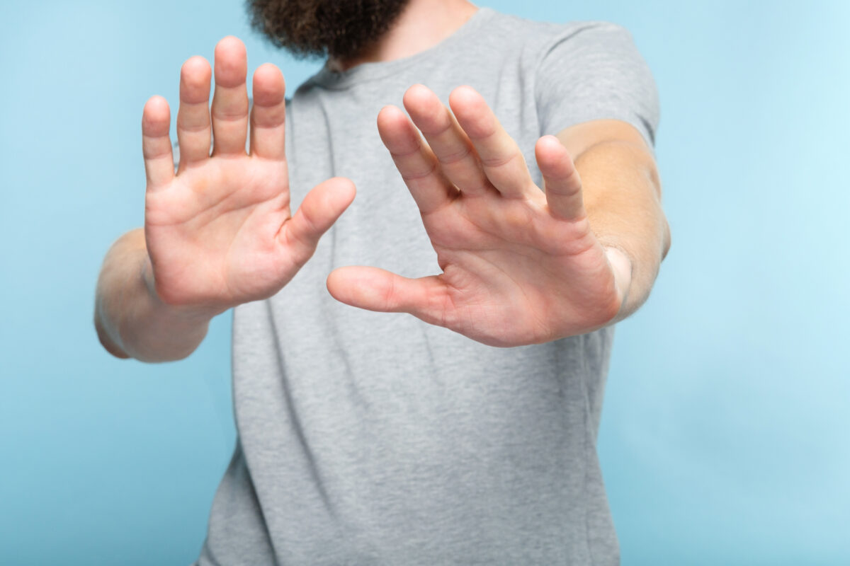 Photo shows a man holding his hands up, palms out, towards the camera. Vegans use several different types of social skills to adapt and “survive” difficulties in a predominantly meat-eating world