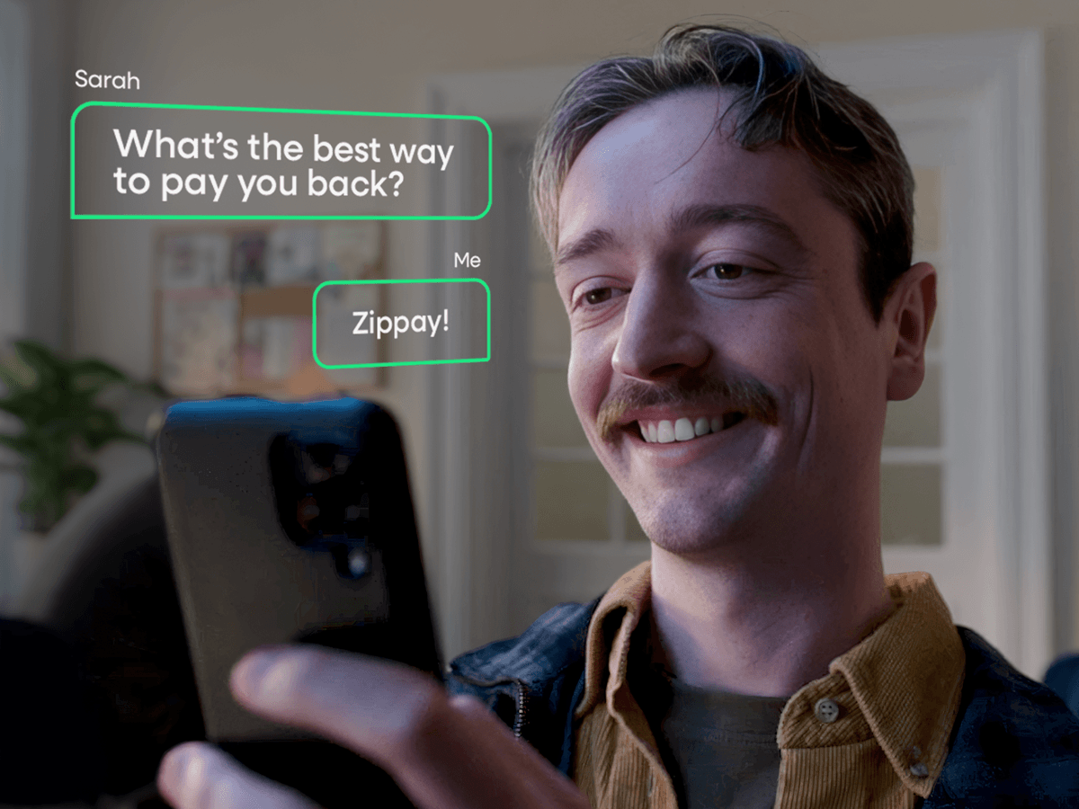 A man looking into a smartphone with text bubbles beside him that read "What's the best way to pay you back?" "Zippay".
