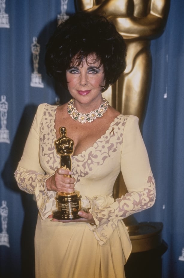 Elizabeth Taylor, wearing a pale yellow outfit with sheer detail on the sleeves and along the collar, with a floral necklace, in the 65th Academy Awards press room at the Dorothy Chandler Pavilion in Los Angeles, California, 29th March 1993. Taylor holds her Jean Hersholt Humanitarian Awards.