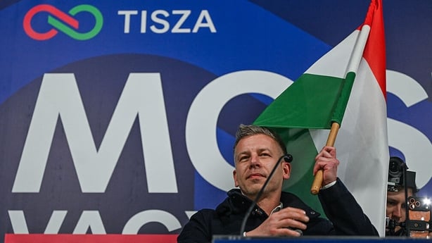 Peter Magyar waves a national flag while standing before a campaign banner