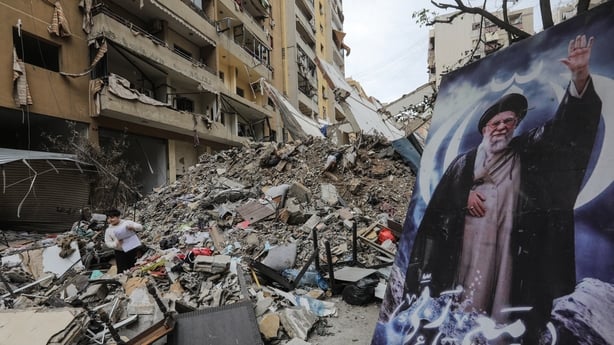 A boy stands amid the debris of a destroyed building next to a portrait of Iran's slain supreme leader Ayatollah Ali Khamenei during a media tour organised by Iran-backed militant group Hezbollah in the Haret Hreik area of Beirut's southern suburbs