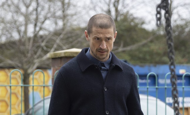 Carl Webster looking confused while standing in front of Debbie, who is on a swing, in Coronation Street.