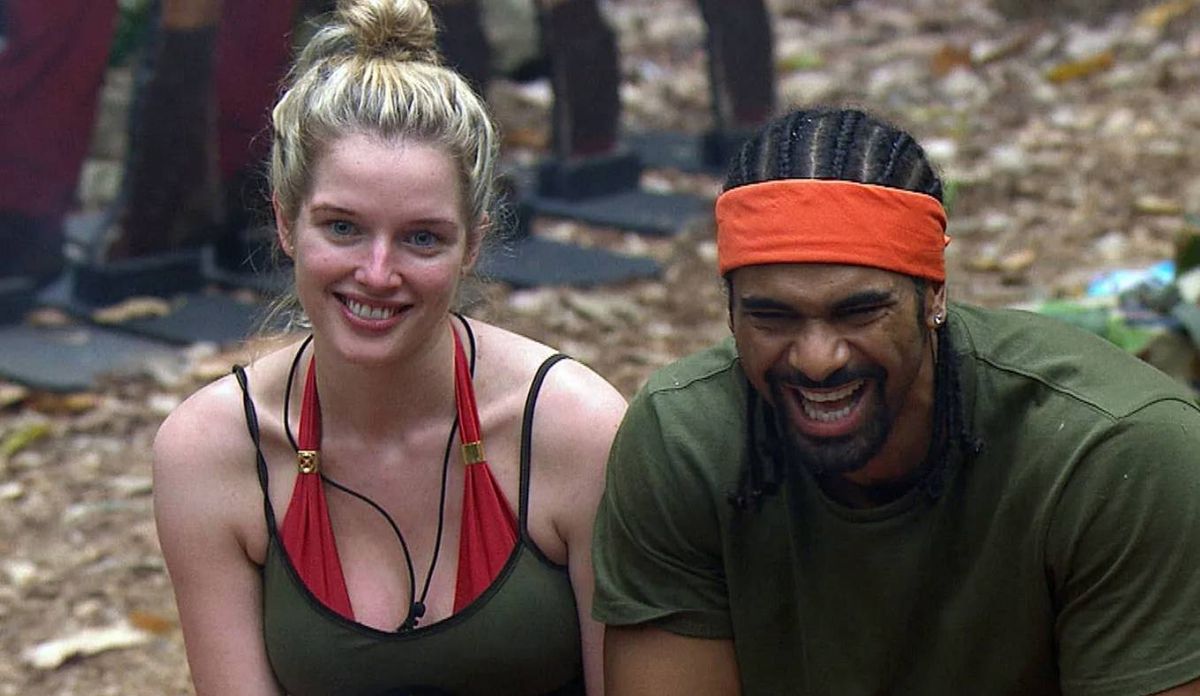 An image depicts two individuals, one wearing a green tank top and an orange headband, and the other in a red and black sleeveless top with a necklace, both smiling and seated in a forested environment.
