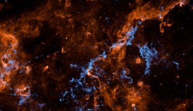 Wispy filaments of vibrant orange and electric blue cosmic dust and gas weave through a dark, star-studded expanse of outer space, creating a chaotic and intricate web of celestial matter.
