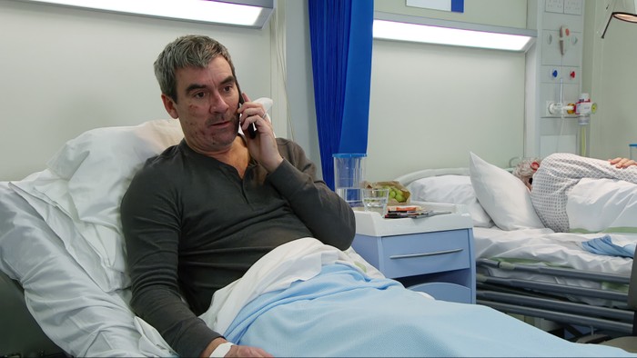 13_04_emm_cain_moira_01 Cain lies in a hospital bed on a phone in Emmerdale