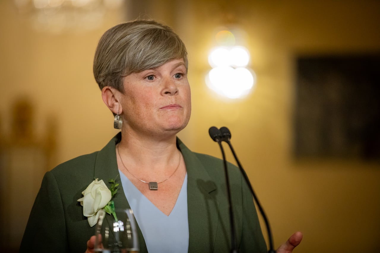 A white woman with short hair and hooped earrings speaks to a mic.