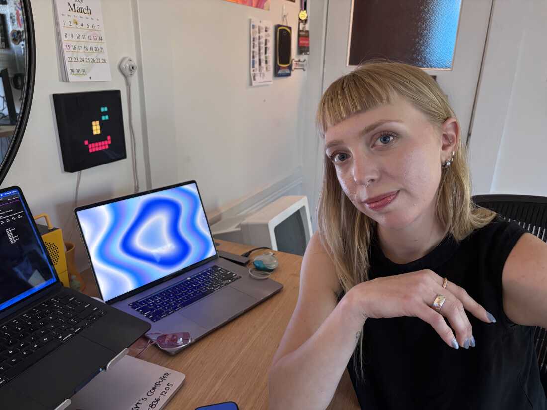 In this photo, digital artist Kyt Janae is sitting at a desk with multiple laptops on it.