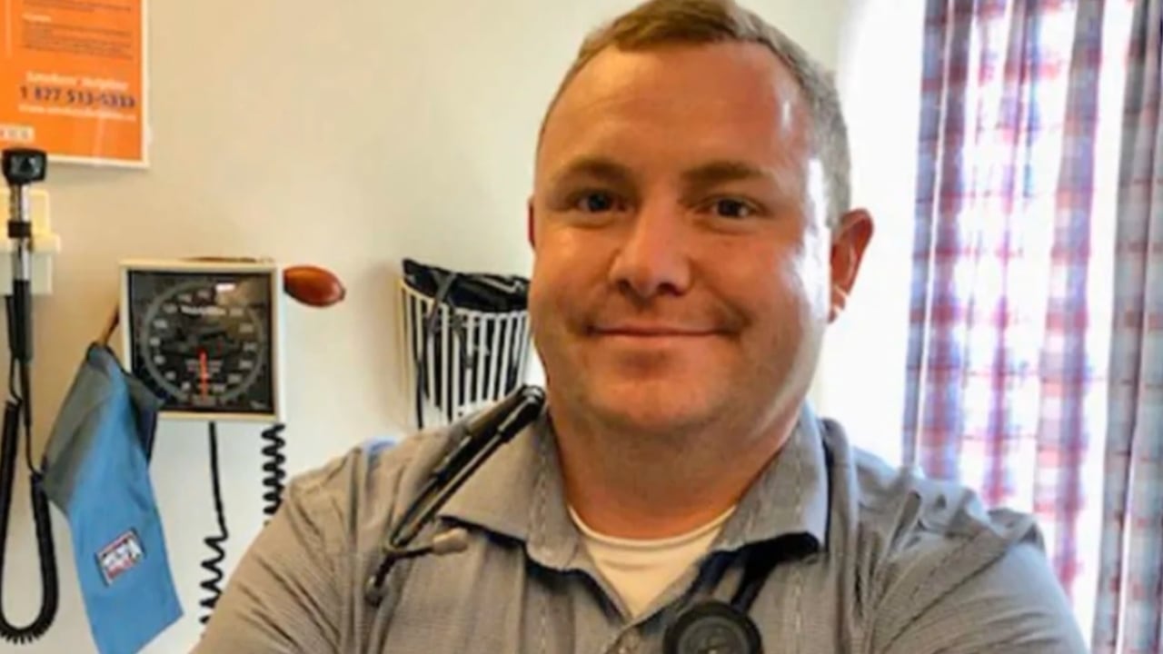 A man with a stethoscope around his neck posing for a photo in a doctor's office.