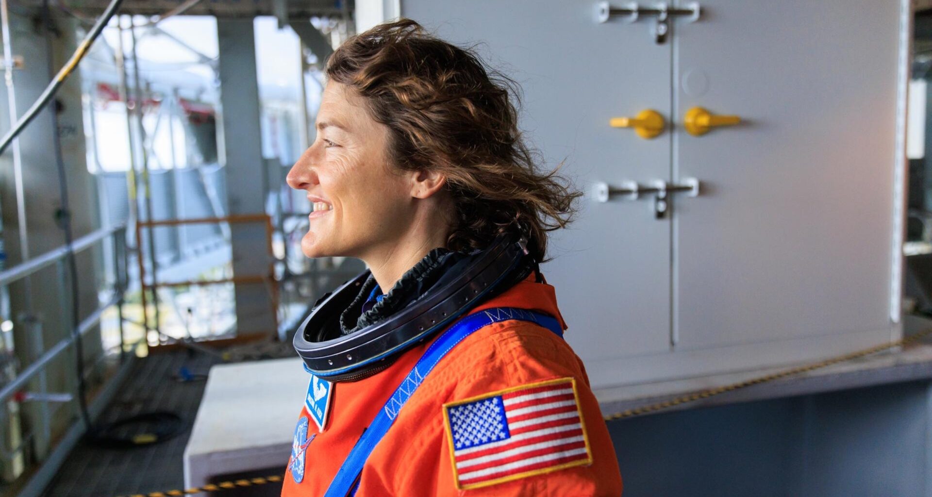 Christina Koch the climber: The astronaut climbs rock and ice on earth. Here she stands and looks out in an orange space suit.