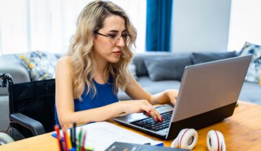 disabled woman sitting in wheelchair at the table and looking at computer monitor.