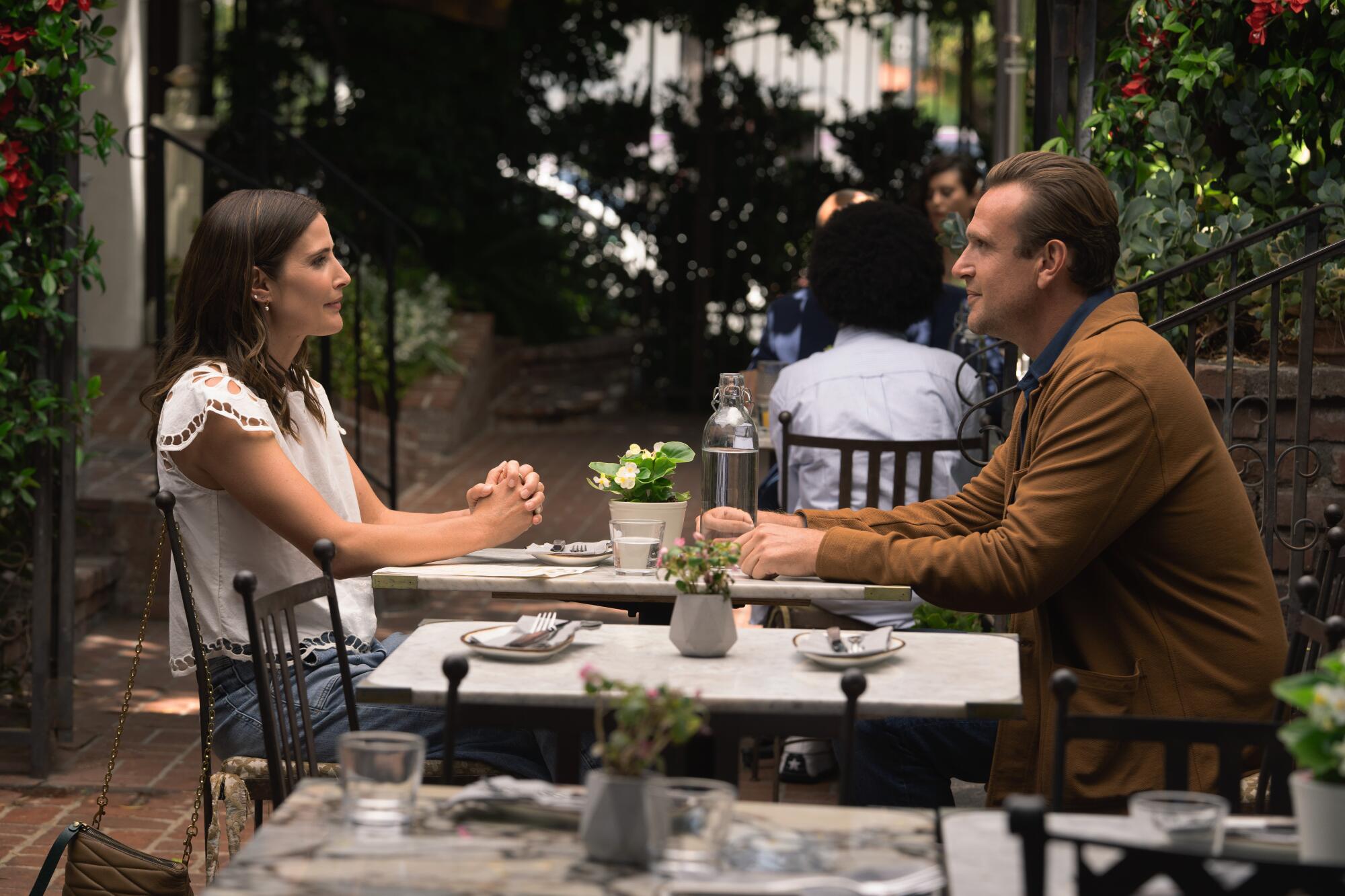 A woman and a man seated outside at a cafe.