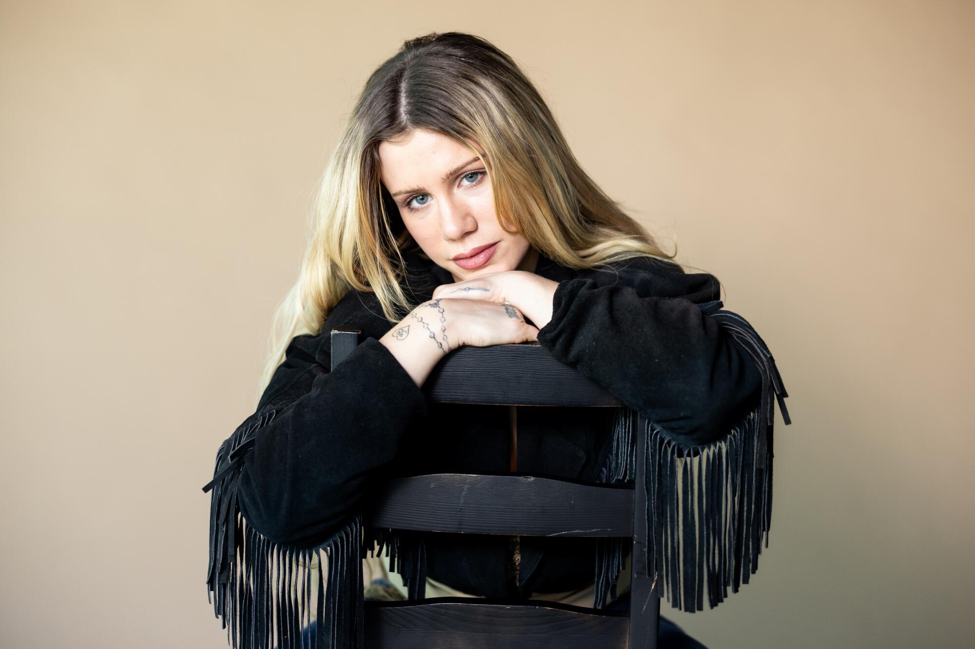 Slayyyter leans against a backwards chair