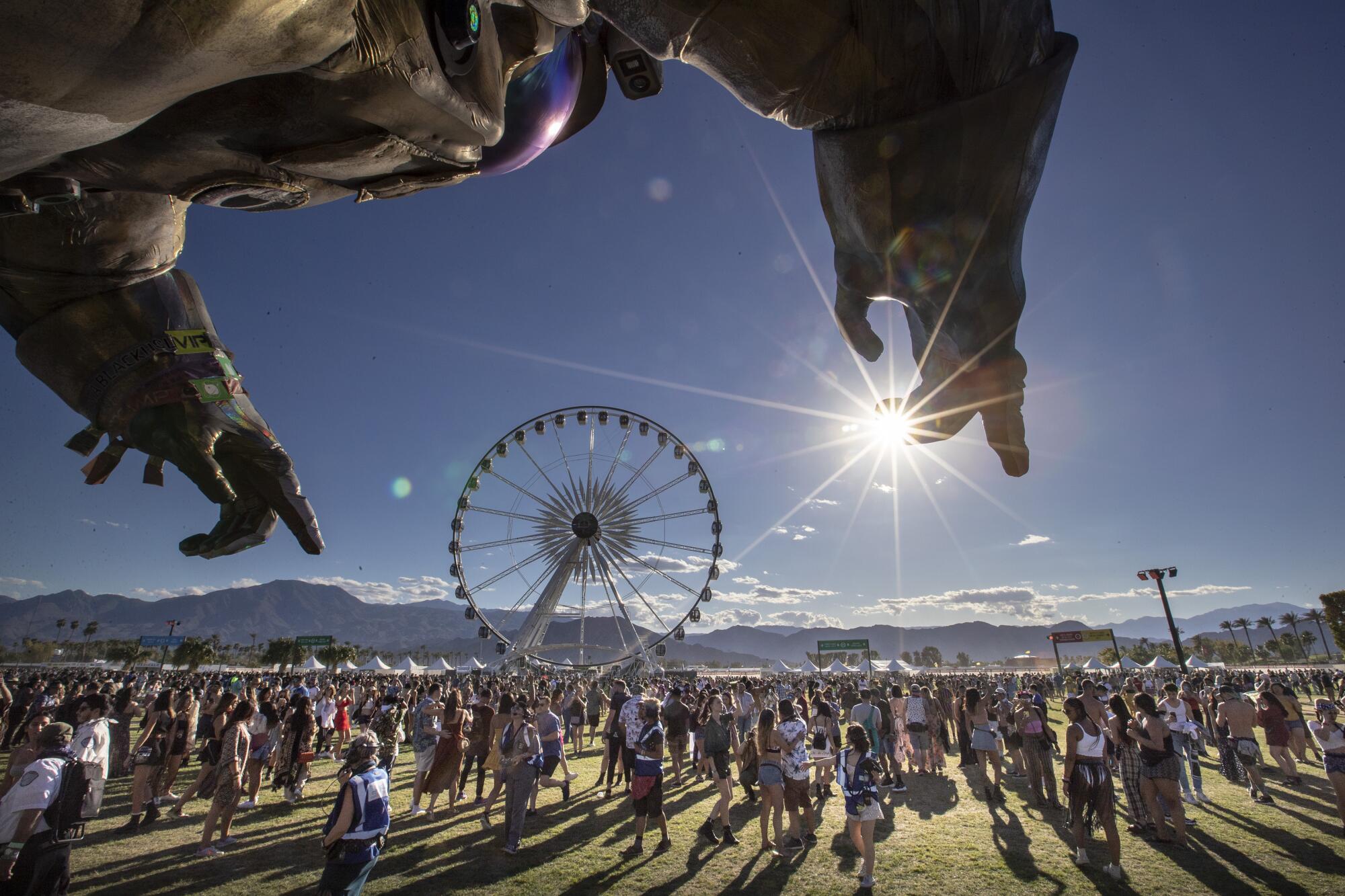 A giant astronaut sculpture points at the sun with a Ferris wheel in the background and hundreds of concertgoers 
