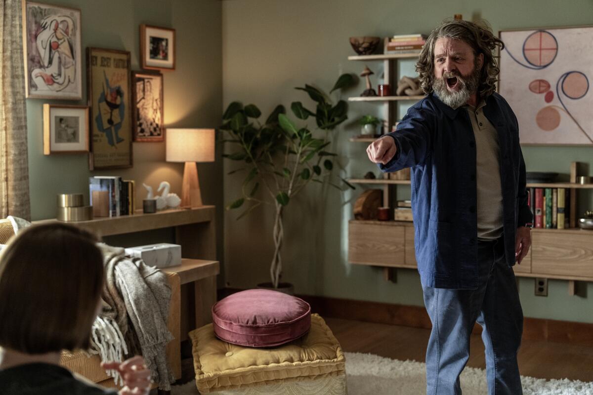 A man in blue jacket stands in a therapist's office and points at her.