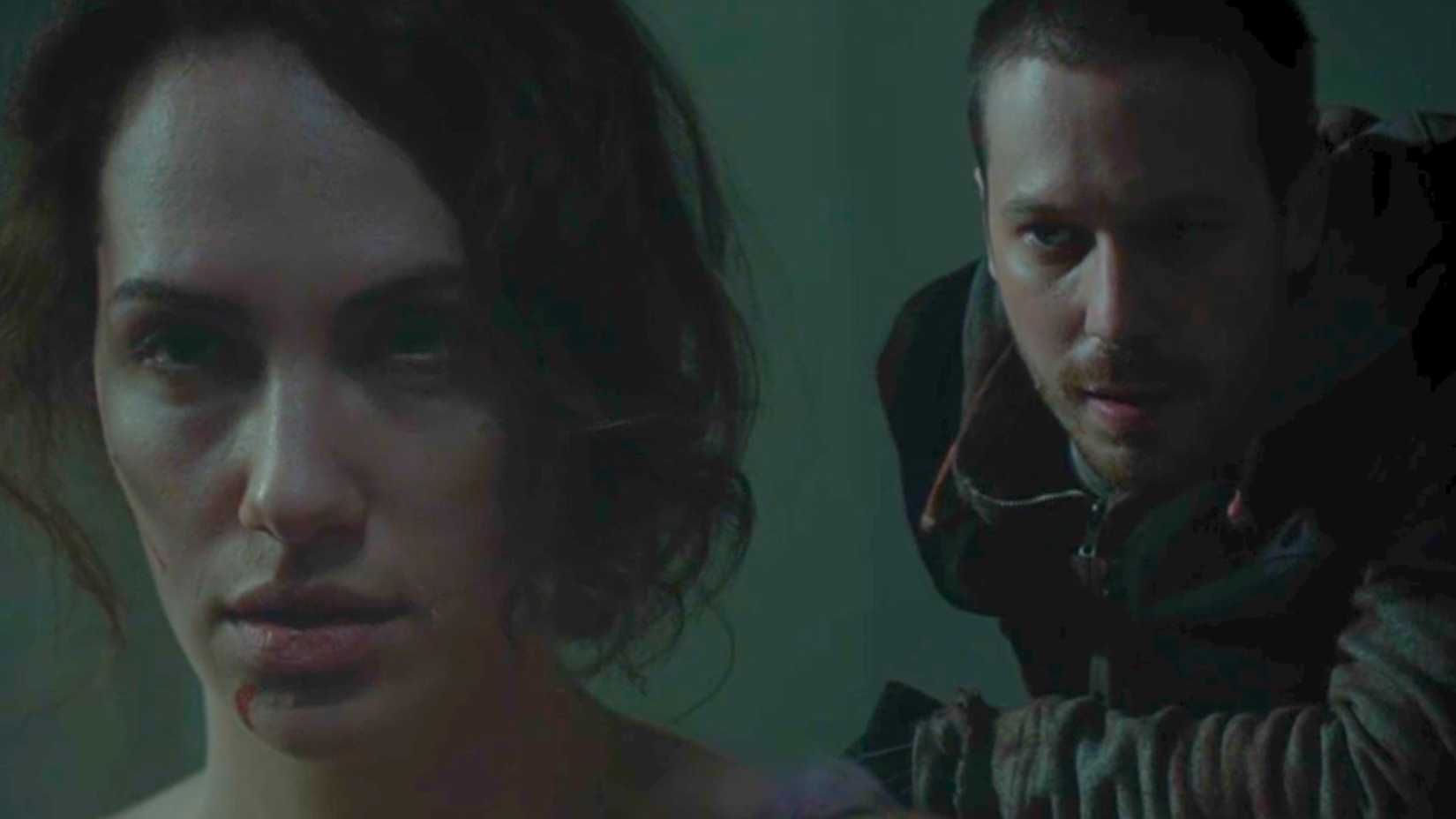 A man in a zipped up hoodie lures behind Maddie Young (Kate Siegel) who is bloodied and bruised.