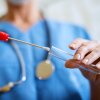 A person in blue medical scrubs holds a test tube and a swab.