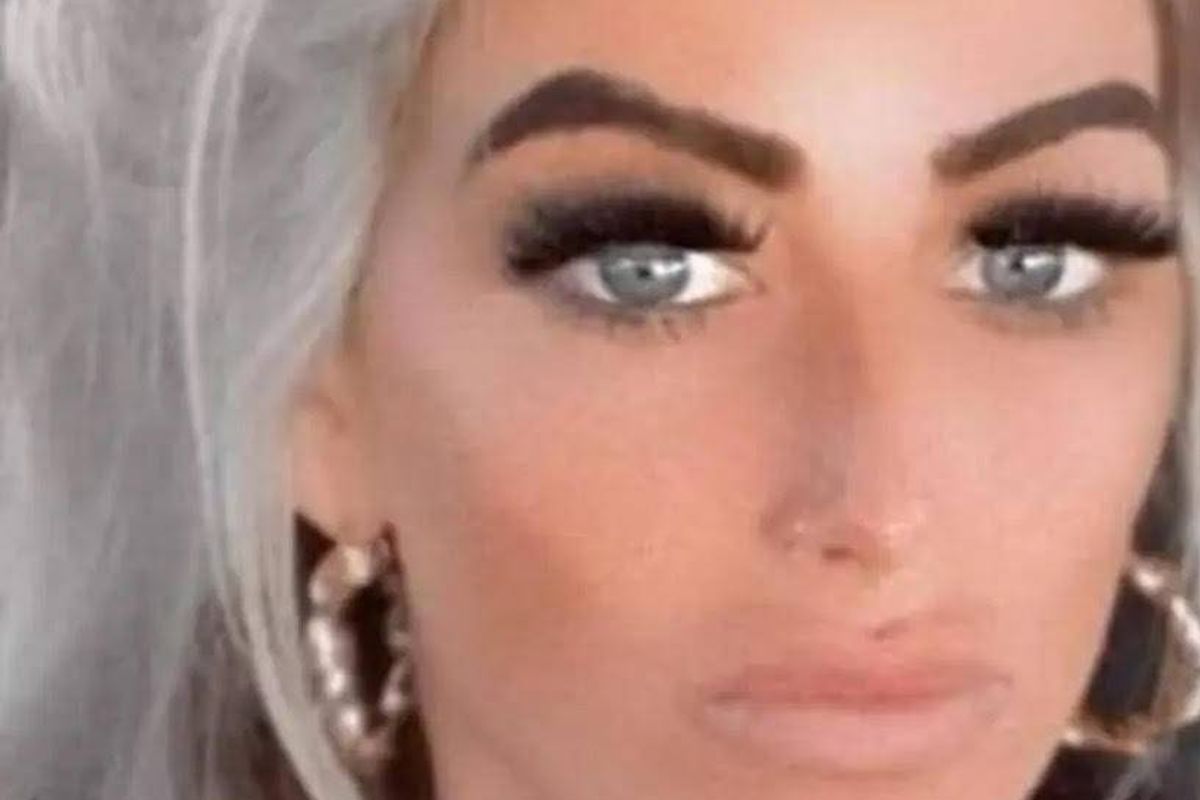 An individual with meticulously styled grey hair and striking blue eyes, accentuated by dramatic eyeliner and earrings, captured in a close-up view.