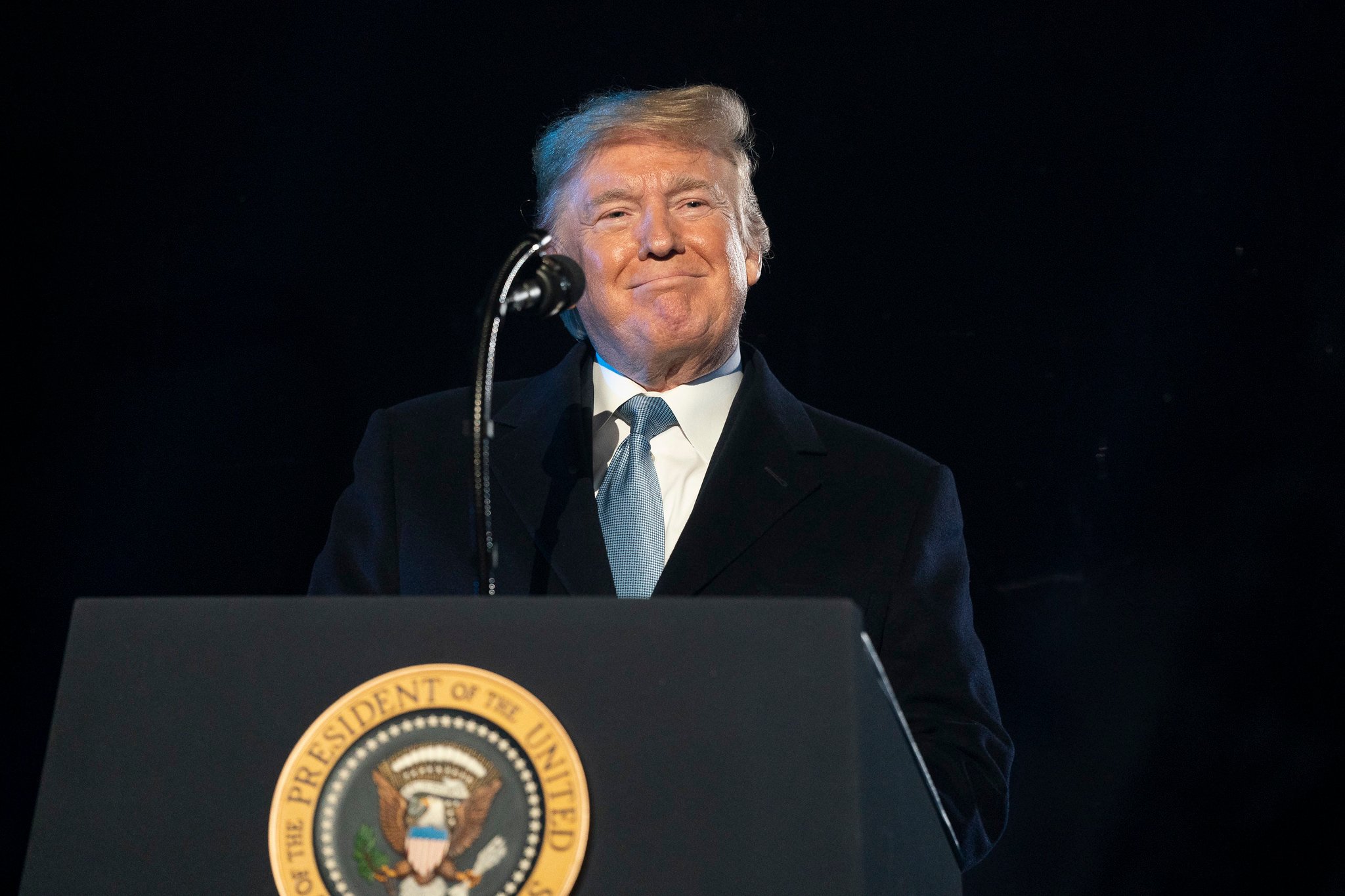 A smiling Donald Trump delivering remarks from behind the presidential podium.