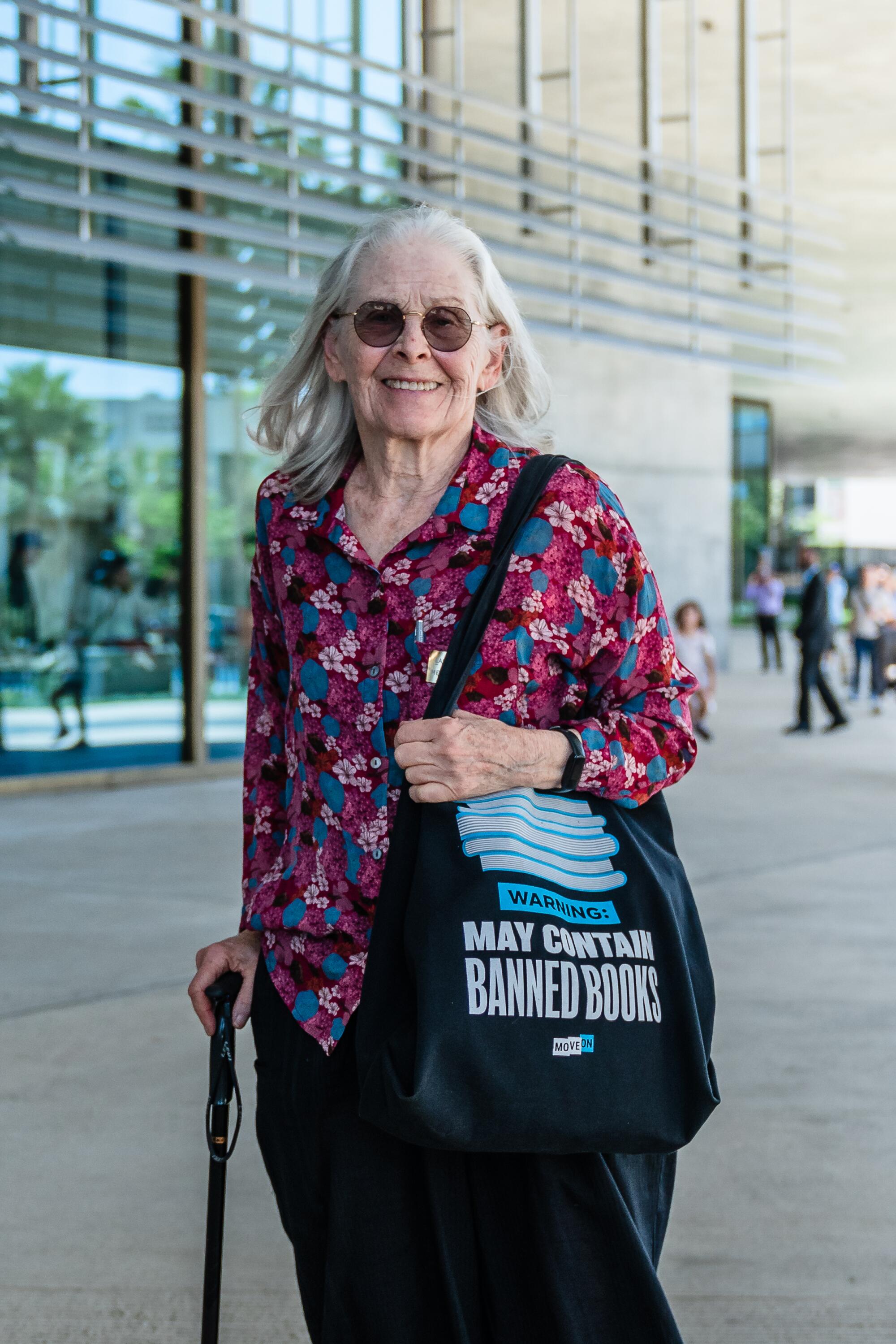 A woman with a cane and tote stands in front of a museum.