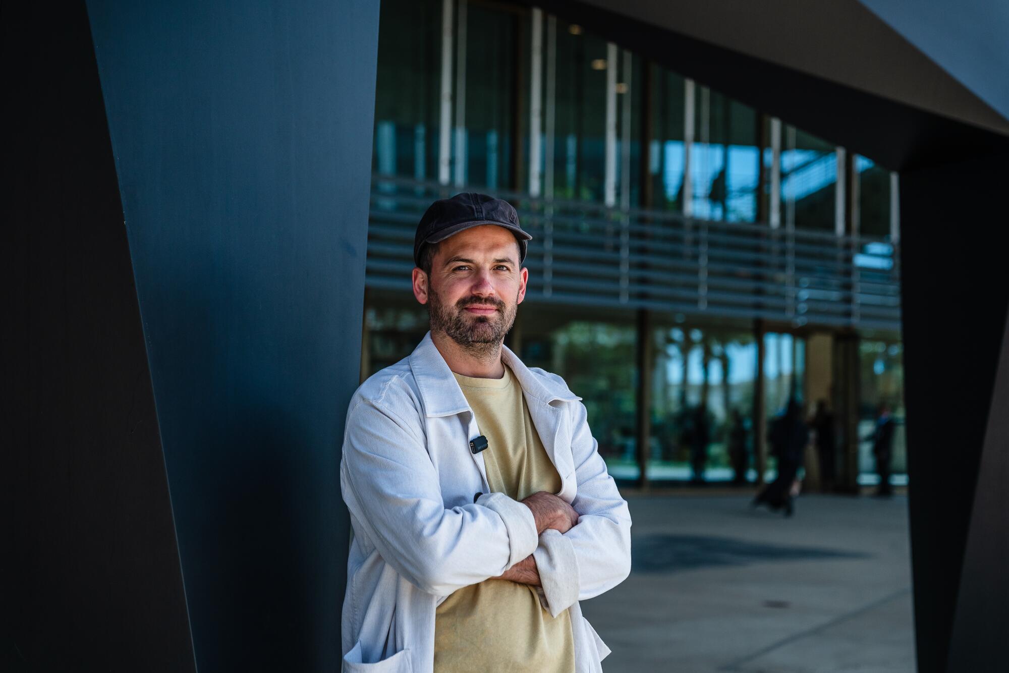 A man stands with his arms crossed in front of a museum.
