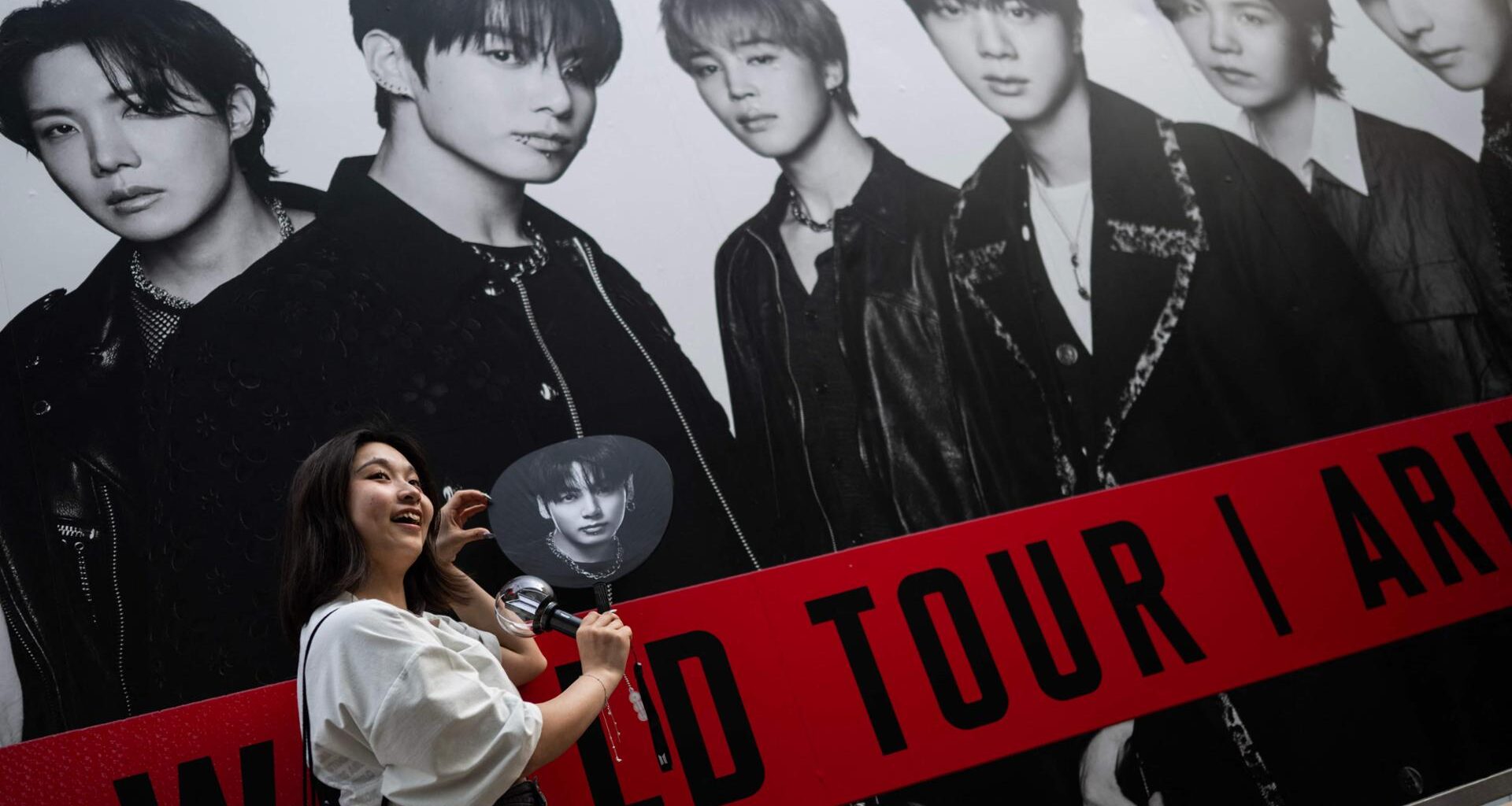 A fan of BTS poses in front of a poster at Tokyo Dome before the start of the K-pop band