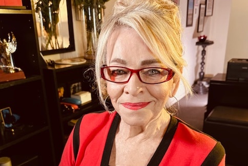 An older woman with blonde hair and red glasses.