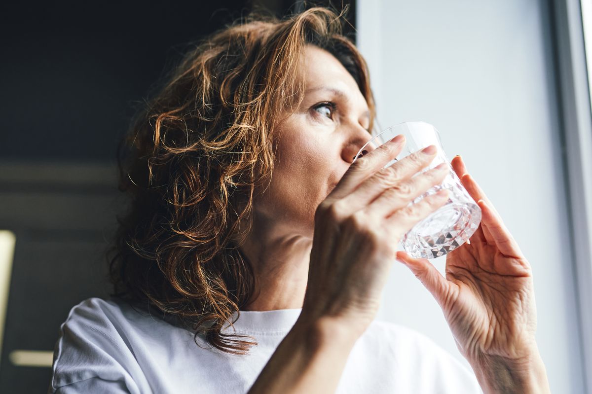 Woman drinking fresh water from a glass, promoting health and wellness