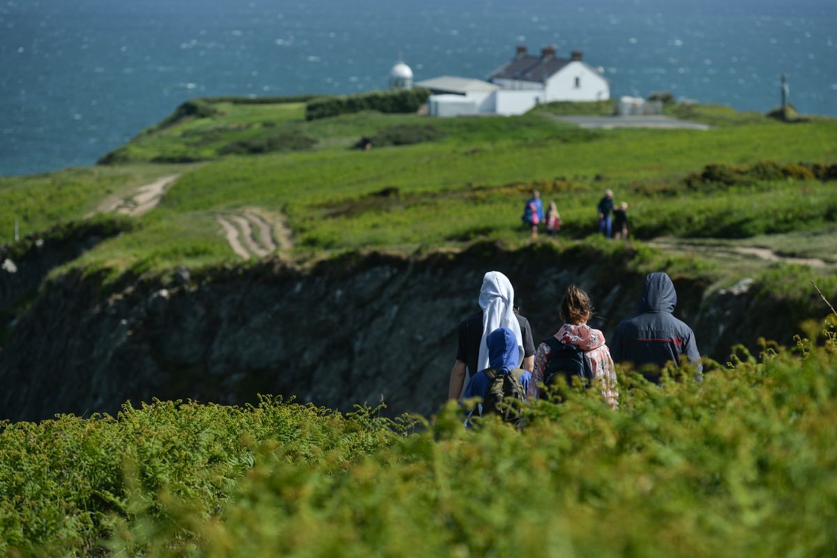 People enjoy nice weather and the Howth cliff path loop walk with the lighthouse and the Irish sea in the background